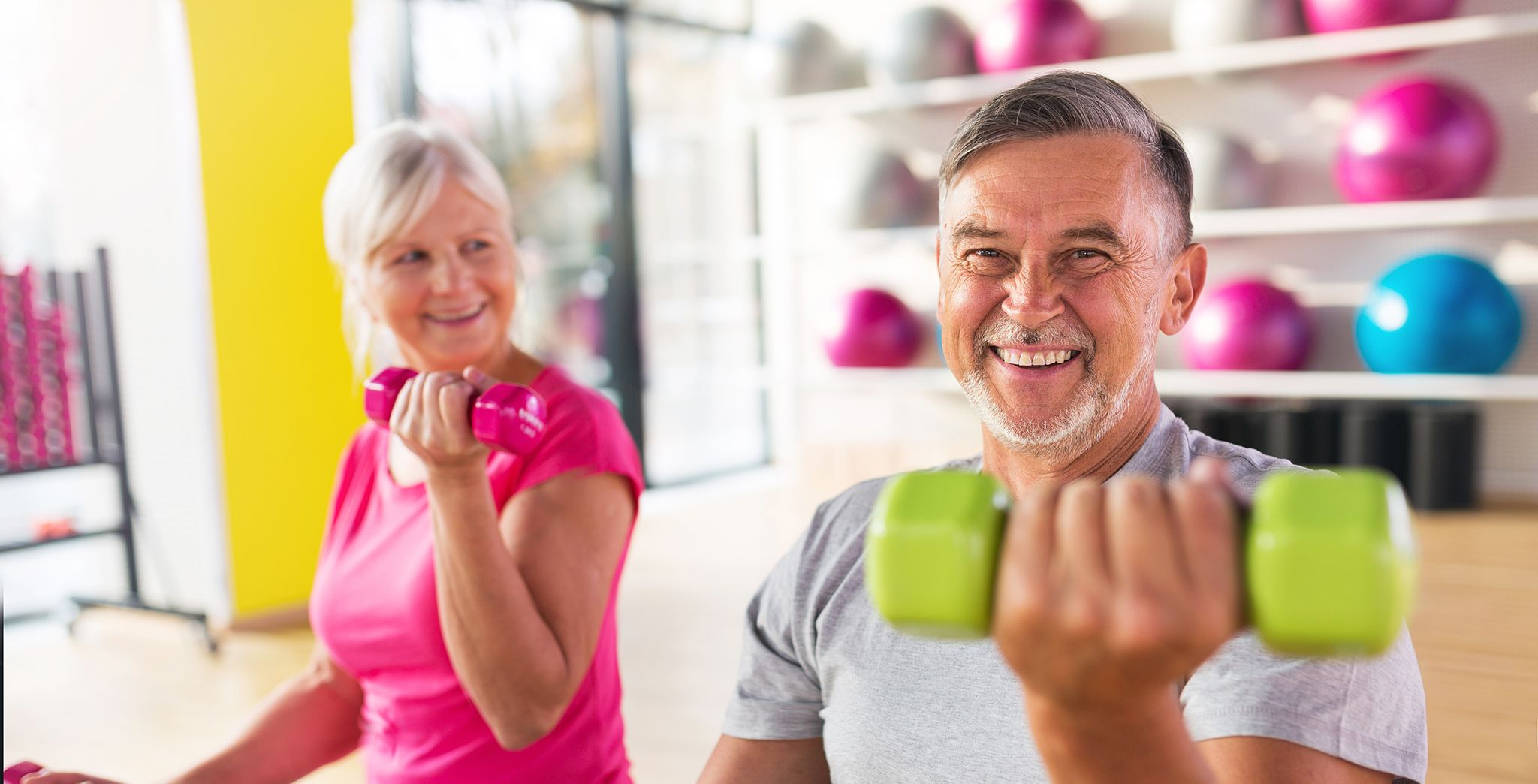 An older man and woman working out with colorful hand weights