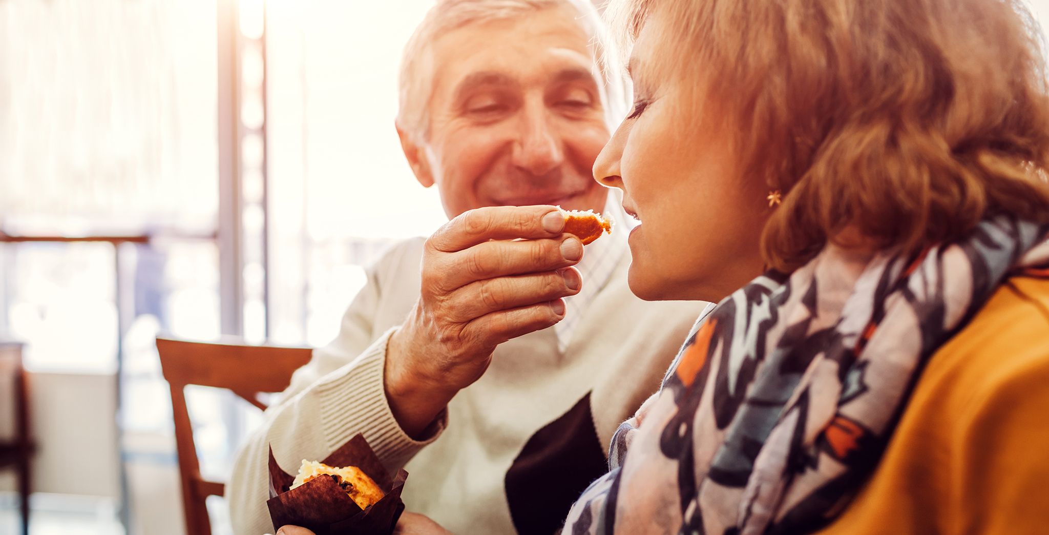 Close up of an older couple, the man is feeding a bite of food to the woman